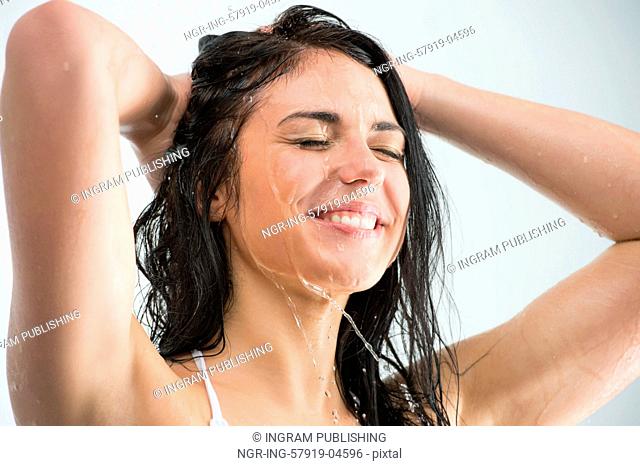 Woman washing her head while showering with happy smile and water splashing. Beautiful Caucasian female model home in shower cabin