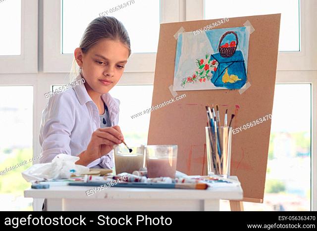 girl sits behind an easel and washes her brush in a glass of water