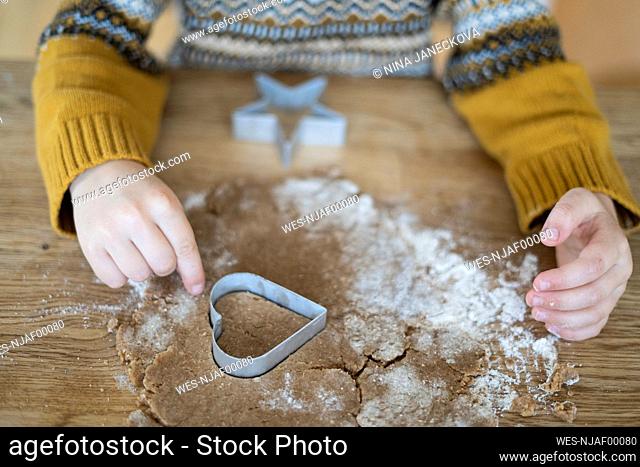 Hands of boy cutting out cookie with heart shaped cutter on table