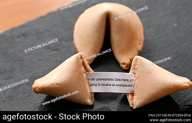 ILLUSTRATION - 07 November 2023, Baden-Württemberg, Stuttgart: A fortune cookie with a note inside saying ""Received an unexpected gift"" lies on a table