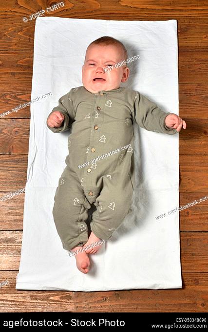high angle view of a baby on the parquet floor dressed, crying and looking at the camera