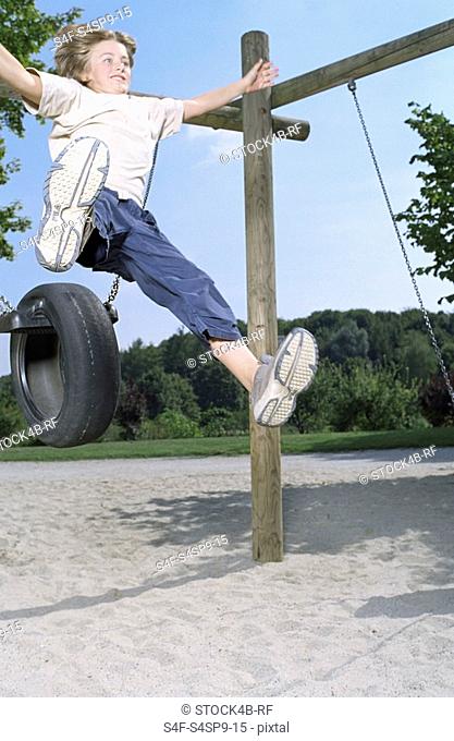Blonde boy jumping from a Rubber Tire-Swing - Playground - Fun - Courage - Freedom