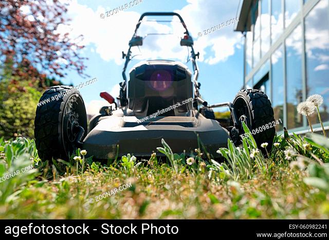 Front low angle shot of blurred high grass with mowing machine on sunny day in a garden