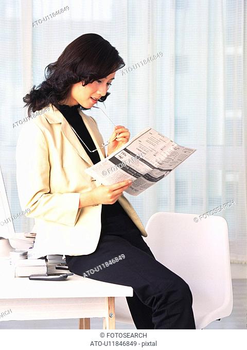 Image of a Business Woman Sitting on a Desk Reading a Worksheet, Side View