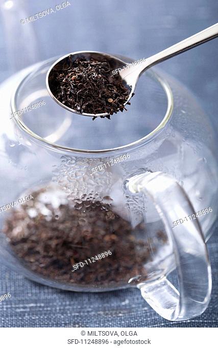 Tea leaves being placed into a glass teapot