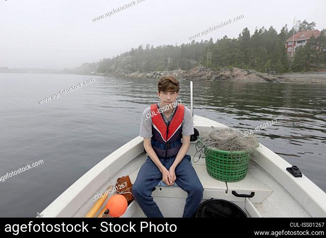 Boy sitting in boat on foggy lake