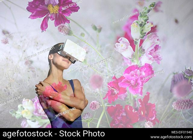 Young woman with virtual reality simulator hugging self amidst flowers