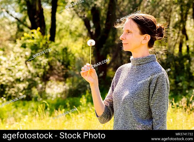 Adult woman blowing the seeds of a dandelion flower at the end of spring near to the forest