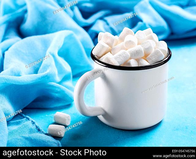 Marshmallows in cup on blue background with copyspace. Winter food background concept