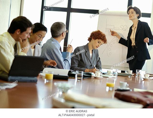 Group of business people in conference room, businesswoman pointing at presentation board