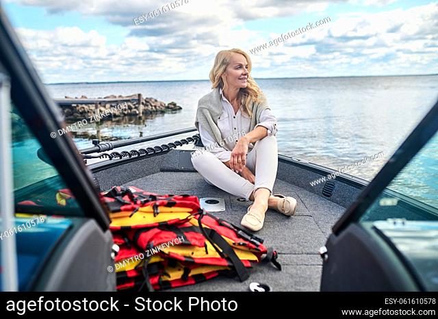 A boat trip. A blonde mature woman in white clothes sitting on a boat and looking dreamy