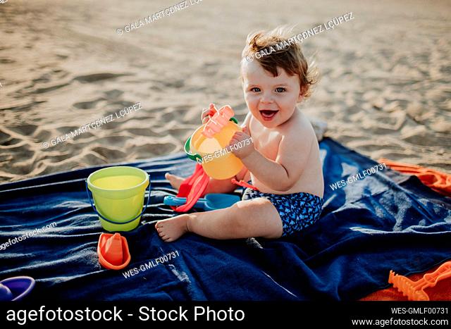 Cheerful cute baby boy playing at beach during sunset on sunny day