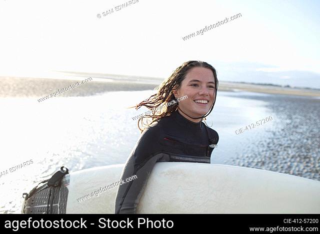 Happy young female surfer with surfboard on sunny ocean beach