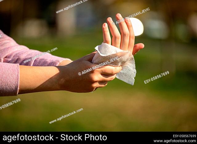 Cleaning fingers and hands with wet wipes outdoor against disease infection versus flu or infulenza, blurred green background