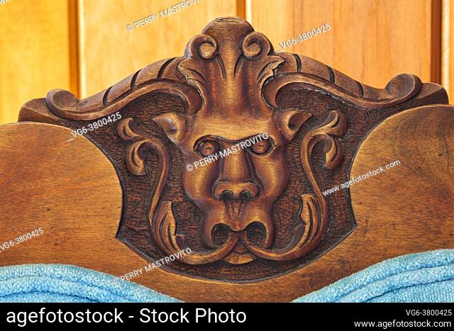 Close-up of carved gargoyle's head on backrest of blue velvet upholstered antique walnut wood chair in hallway on upstairs floor inside an old 1807 rcottage...
