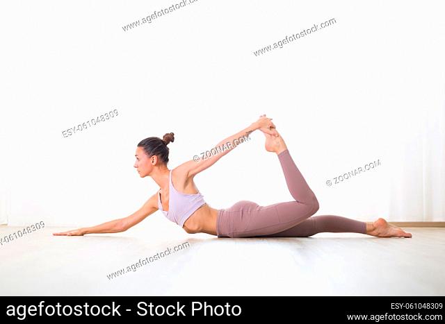 Portrait of gorgeous active sporty young woman practicing yoga in studio. Beautiful girl practice Dhanurasana half bow yoga pose