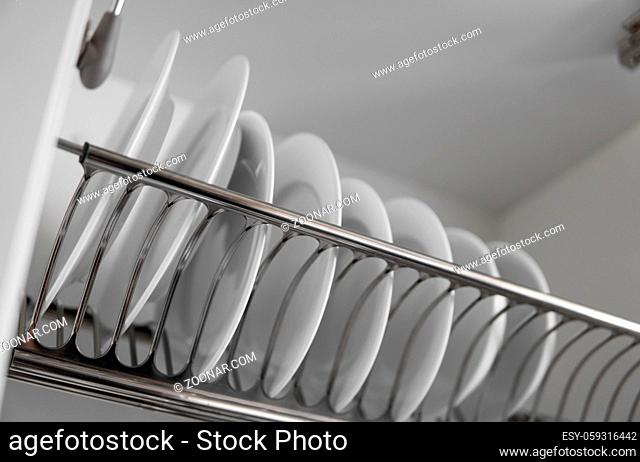 Dish drying metal rack with big nice white clean plates. Traditional comfortable kitchen. Open white dish draining closet with wet dishes of glass and ceramic