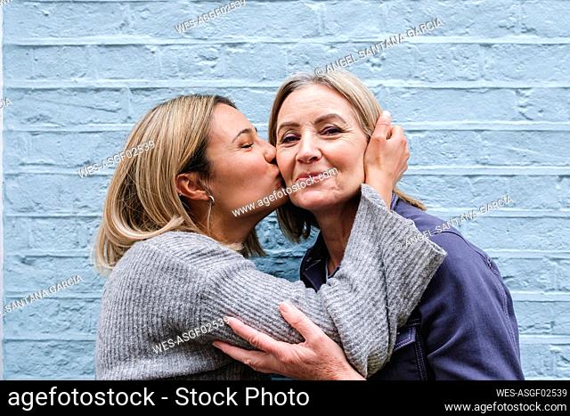 Young woman kissing mother in front of blue wall