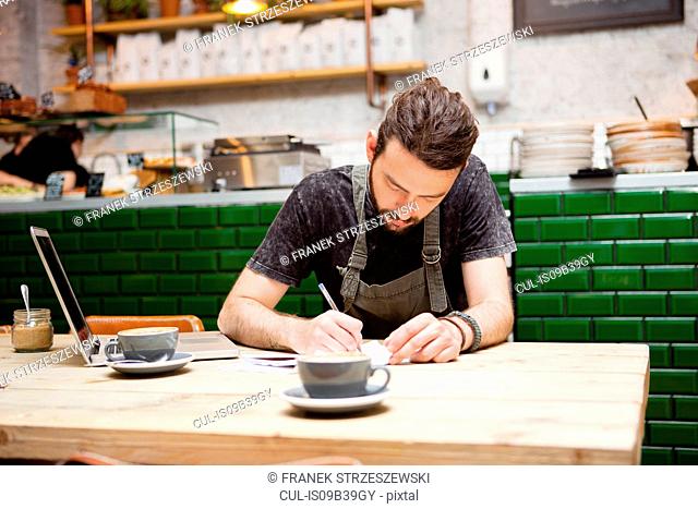 Young male cafe owner doing paperwork at table