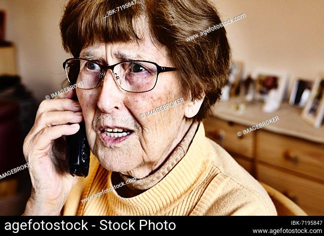 Senior citizen at home looking startled while phoning, grandson trick, Cologne, North Rhine-Westphalia, Germany, Europe