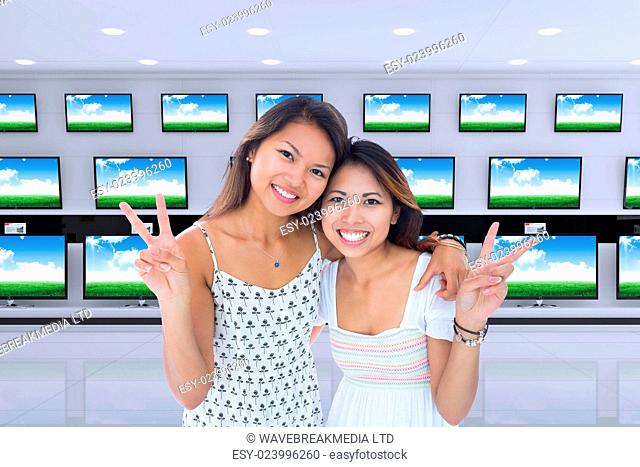 Two smiling young women making a peace gesture against televisions for sale