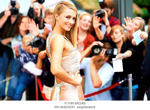 A stunning actress walking the red carpet at her movie premiere surrounded by fans and the press