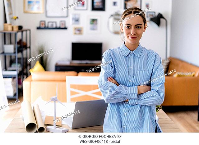 Portrait of confident woman standing in office with wind turbine model on table