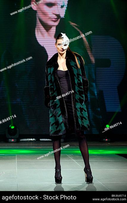 Beautiful fashion model walks on runway in fur coat with online screen on background