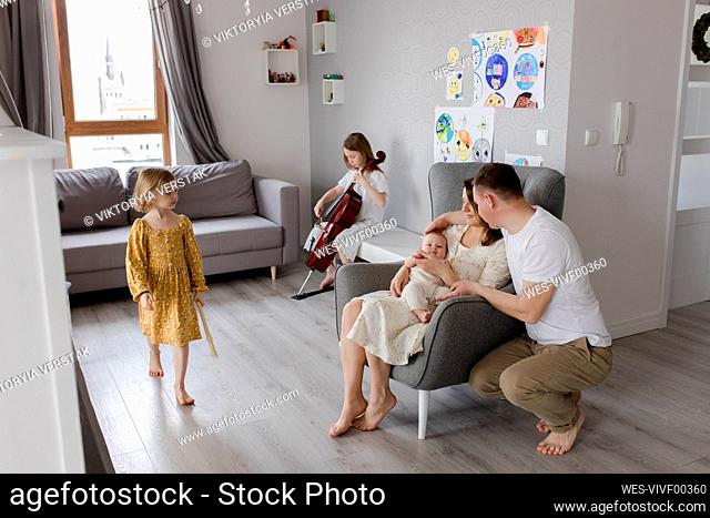 Parents holding boy with girl playing musical instrument in background
