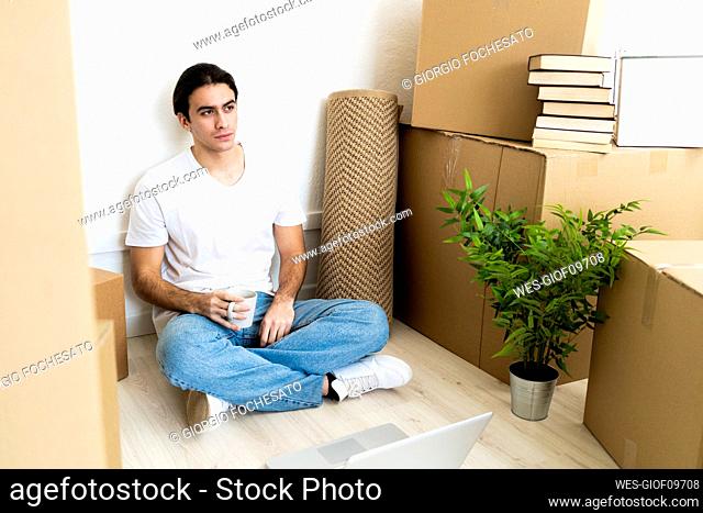 Thoughtful young man holding coffee cup while sitting in new house