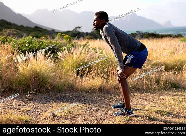 Fit african american man in sportswear resting leaning on knees in tall grass