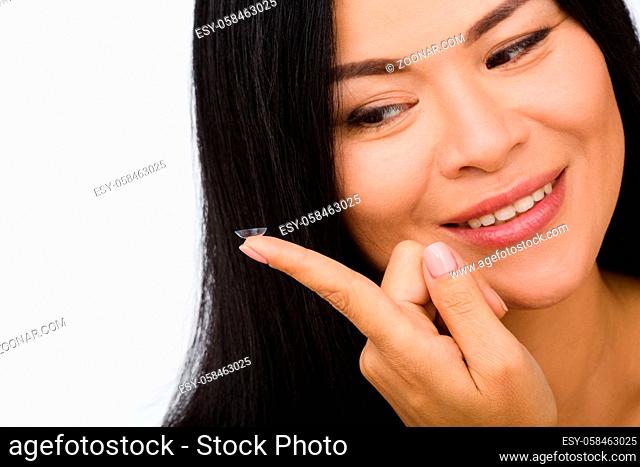 Closeup picture of happy smiling Korean or Asian woman looking at contact lens in front of her. Beauty, vision, eyesight, ophthalmology concepts