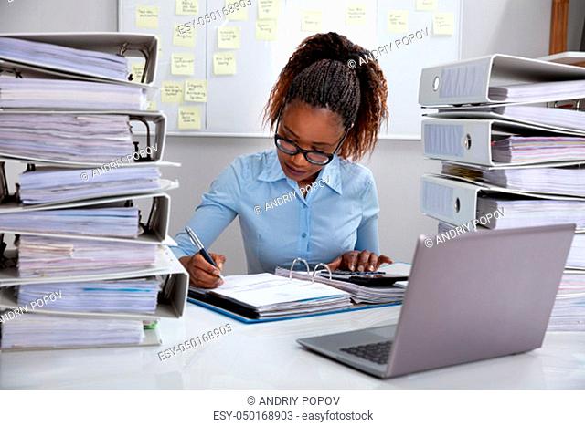 Front View Of Businesswoman Working At Desk With Stack Of Folders In Office