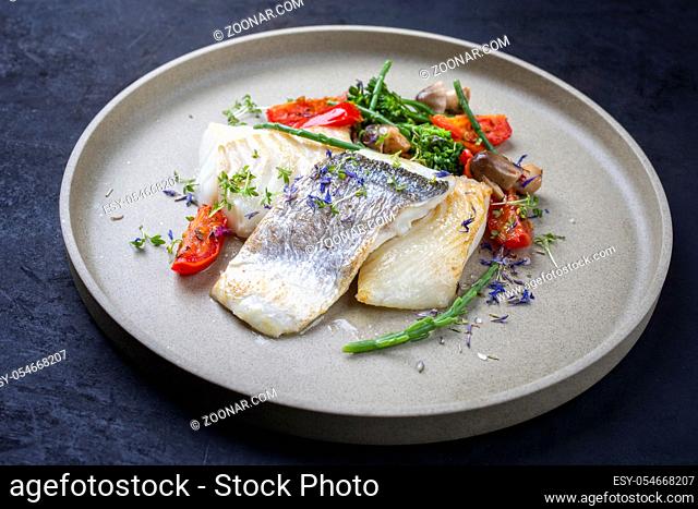 Gourmet fried Italian cod fish filet with broccoli, glasswort and tomatoes as closeup on a modern design plate