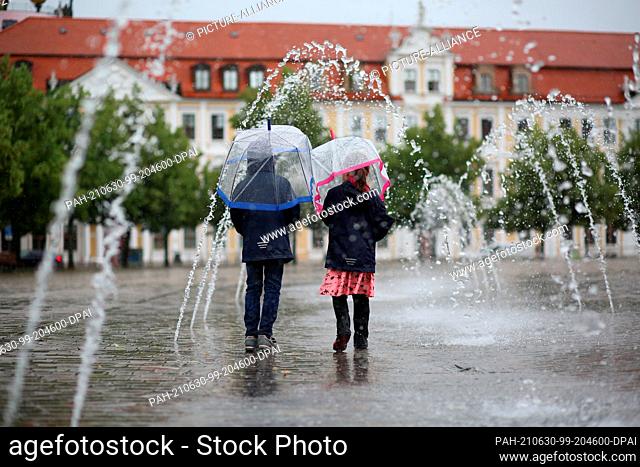 30 June 2021, Saxony-Anhalt, Magdeburg: Two children walk with a sign through a water feature on the Domplatz in rainy weather