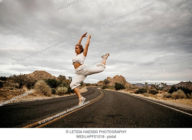Woman jumping on road, Joshua Tree National Park, California, USA