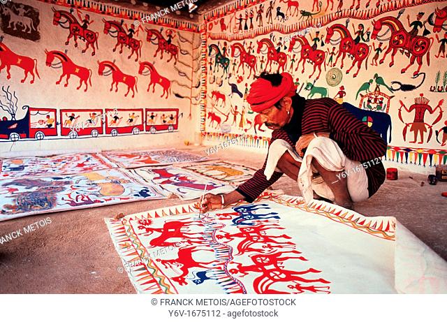 A tribal man ( Bhil tribe) is painting ( Rajasthan, India). This art form is called pithola painting
