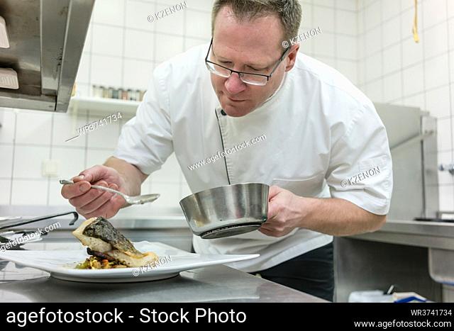 Chef finishing fish on plate in restaurant under pass lamp