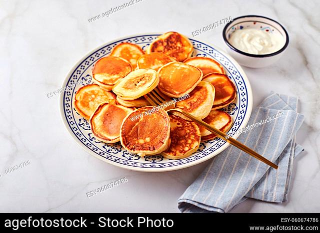 Sweet pancakes with sour cream on a plate on a white table