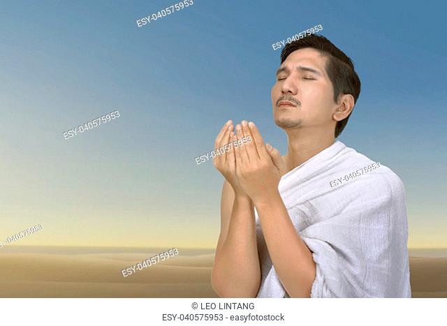 Young asian muslim man praying to god over blue sky background