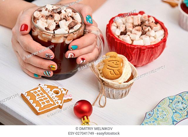 Female hands with bright festive manicure design holding glass mug with hot cocoa and marshmallows. .Handmade ginger cookies, cupcake