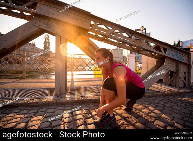 woman tying running shoes laces getting ready to run on city at sunny morning