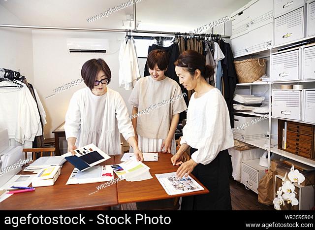 Three Japanese women standing at a table in a small fashion boutique, looking at fabric samples