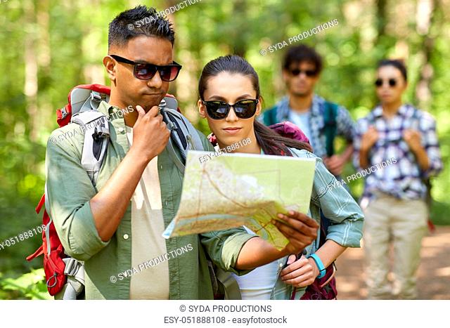 friends with map and backpacks hiking in forest