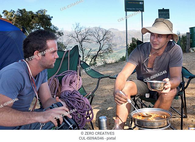 Two young male campers chatting and preparing meal