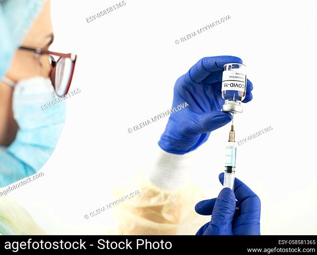 Middle age caucasian female doctor in safety mask glasses and gloves preparing syringe for coronavirus vaccine injection