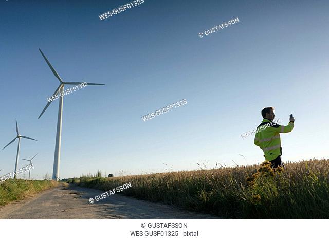 Engineer standing in a field at a wind farm using cell phone