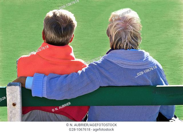 couple of 2 seniors sitting on a bench, in a garden, on a green background, seen from behind, looking in front of them, concept image