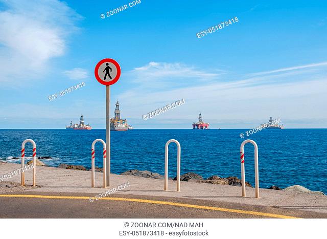 no trespass sign at end of road with ocean background, offshore drilling ships and platform on horizon