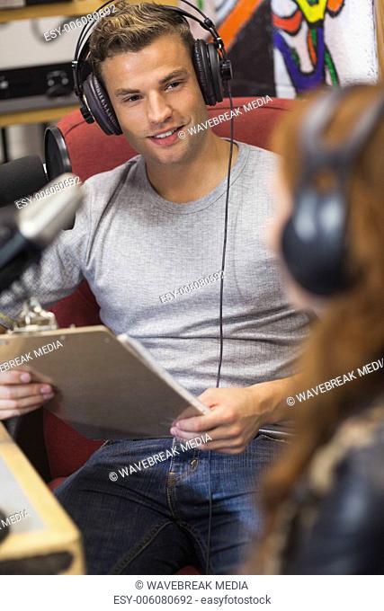 Attractive happy radio host interviewing a guest holding clipboard